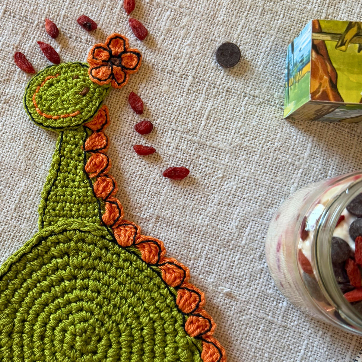 Close-up of the green crochet dinosaur head with an orange flower and embroidered face