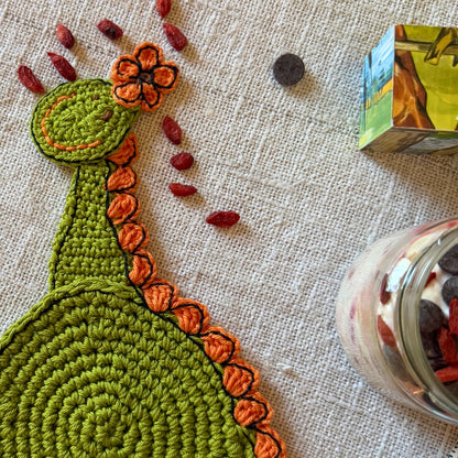 Close-up of the green crochet dinosaur head with an orange flower and embroidered face