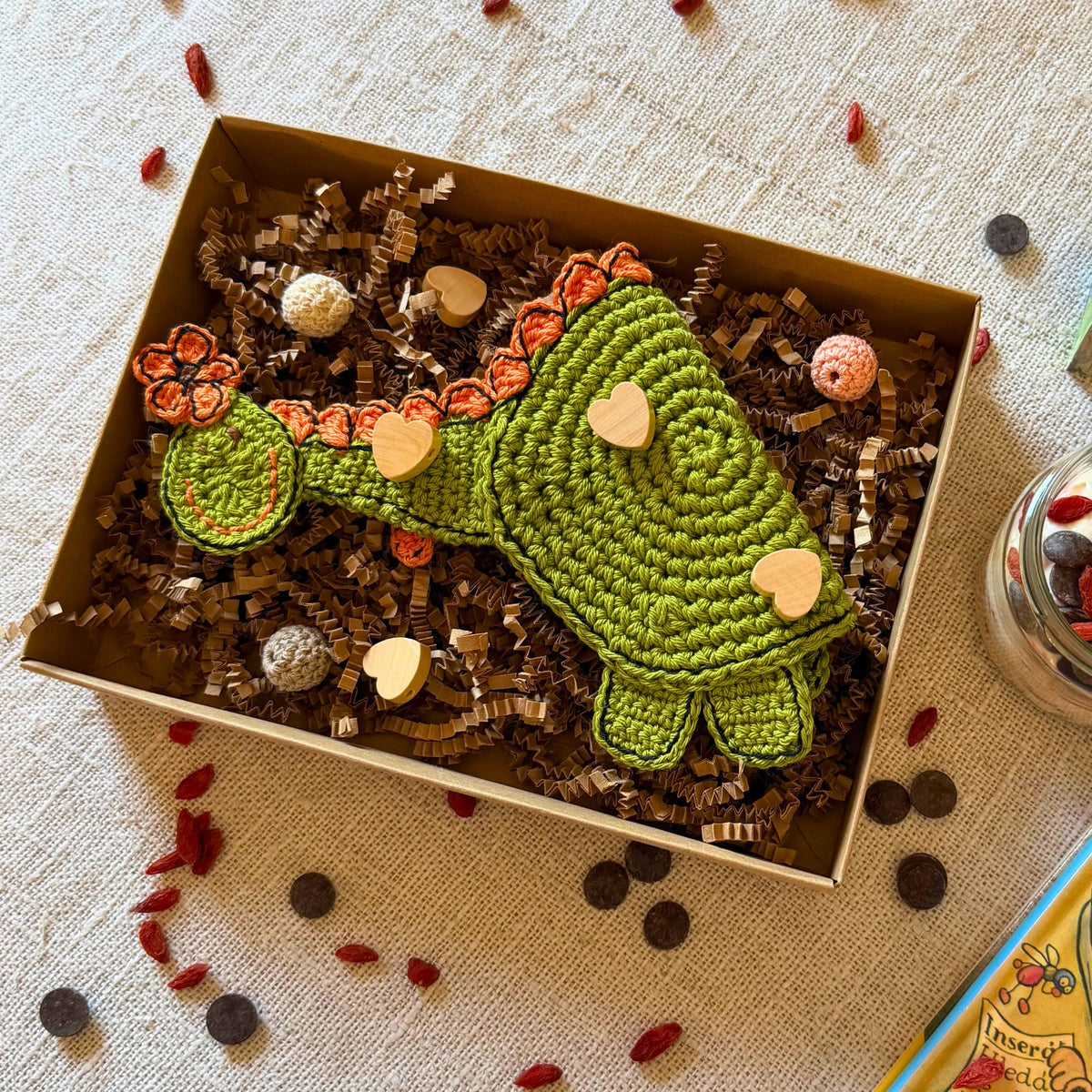 Green crochet dinosaur presented in a kraft gift box