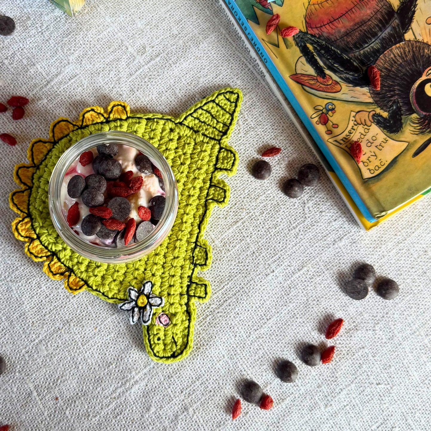 Top view of a glass jar on a green crochet dinosaur coaster with embroidered details and a flower.