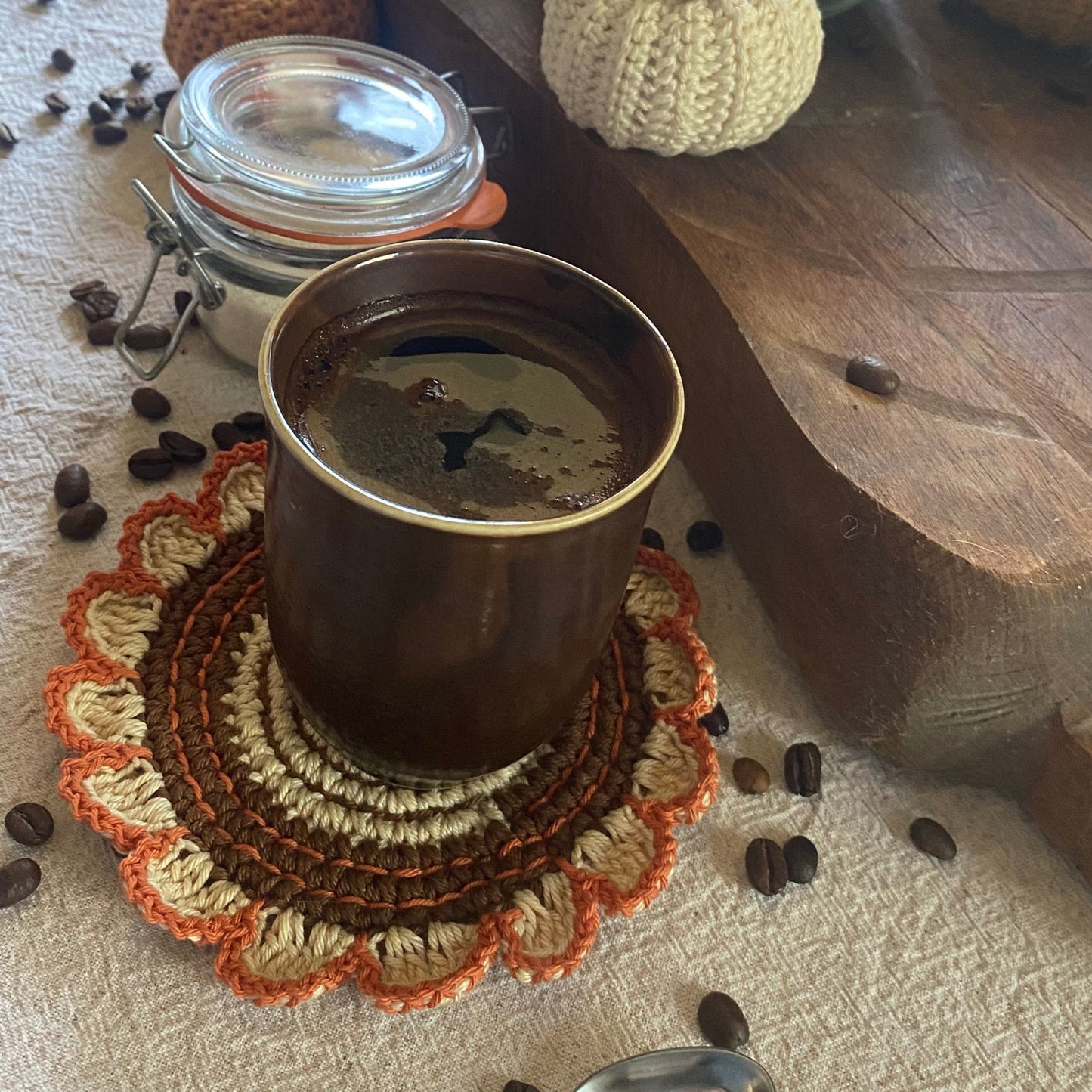 Coffee cup on a textured coaster with coffee beans around on a wooden surface