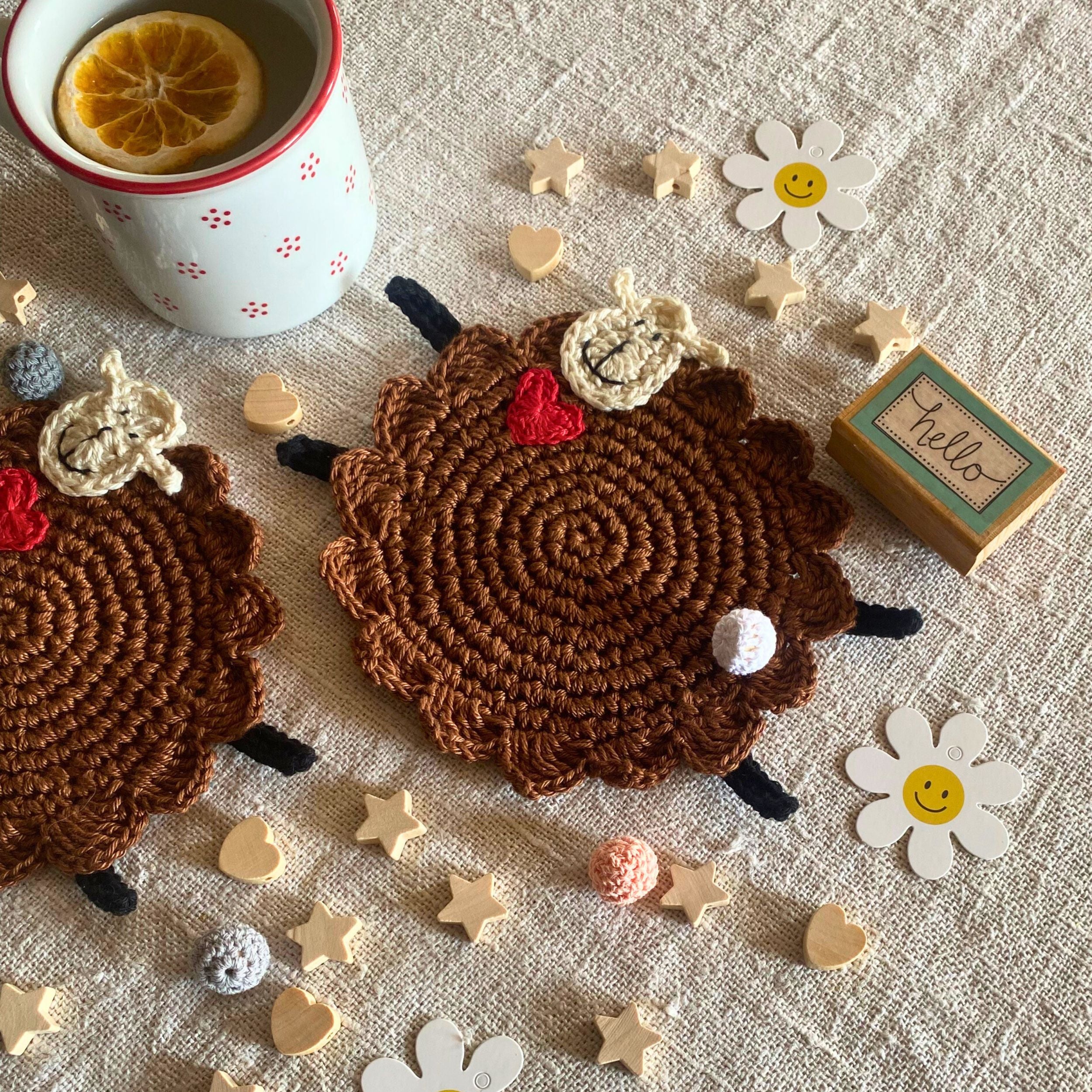 Two handmade brown crochet sheep mug rugs styled with a tea mug on beige linen