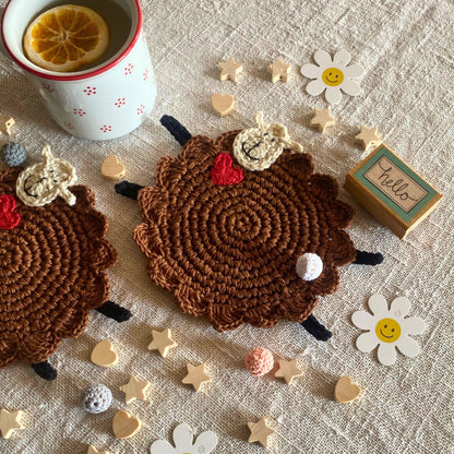 Two handmade brown crochet sheep mug rugs styled with a tea mug on beige linen