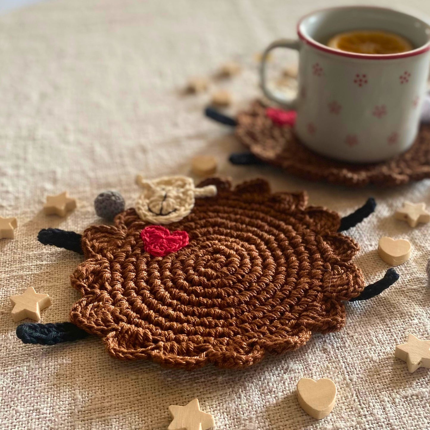Brown crochet sheep mug rug in soft natural light with tea mug in the background