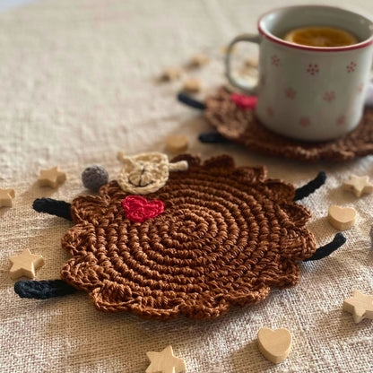 Brown crochet sheep mug rug in soft natural light with tea mug in the background