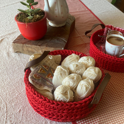 Red crochet basket with yarn balls on a table.