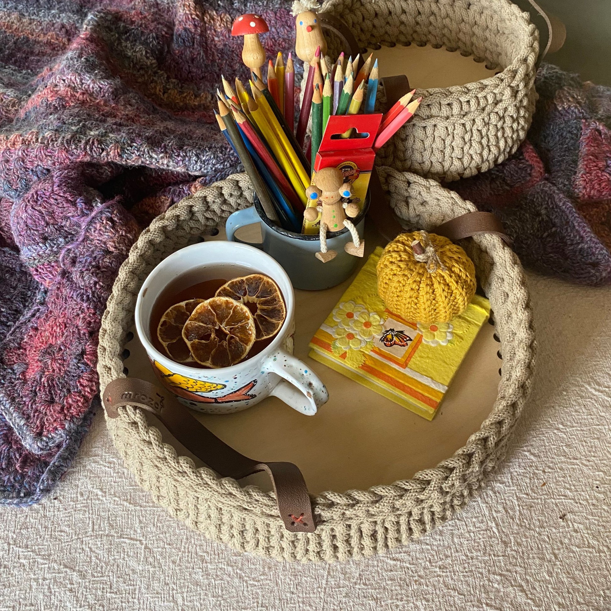 Cup of tea with dried oranges, pencils, and a small notebook on a crochet tray.