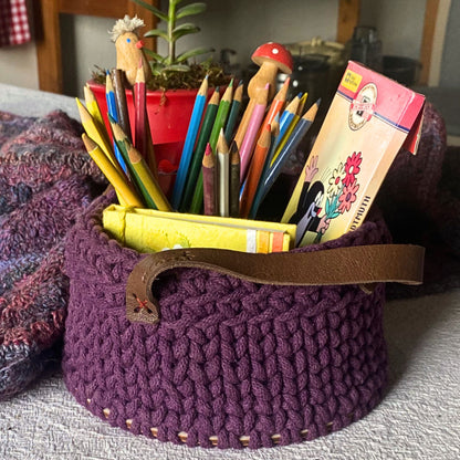 Purple crochet basket filled with colorful stationery items .