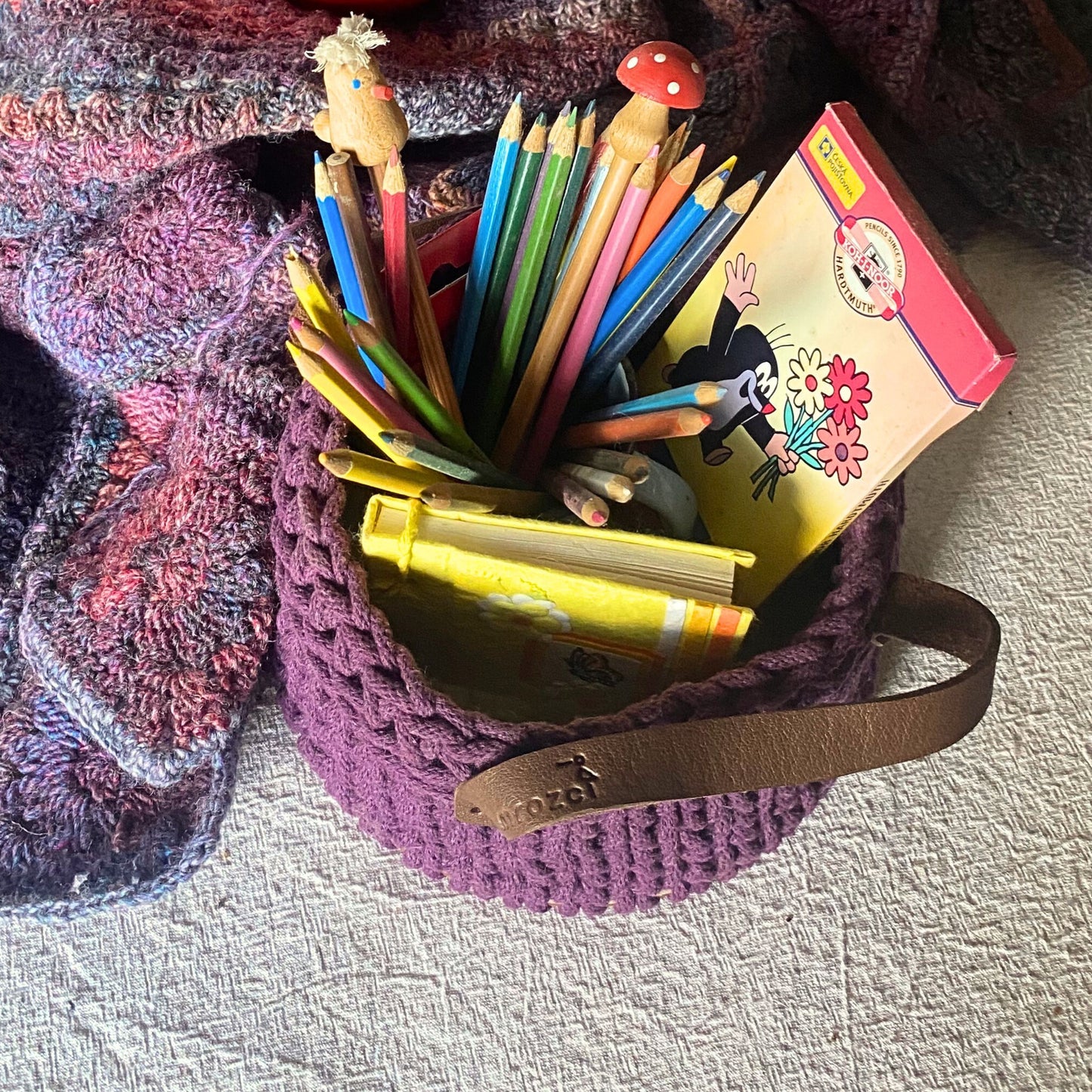 Colorful pencils in a purple crochet basket with leather handles